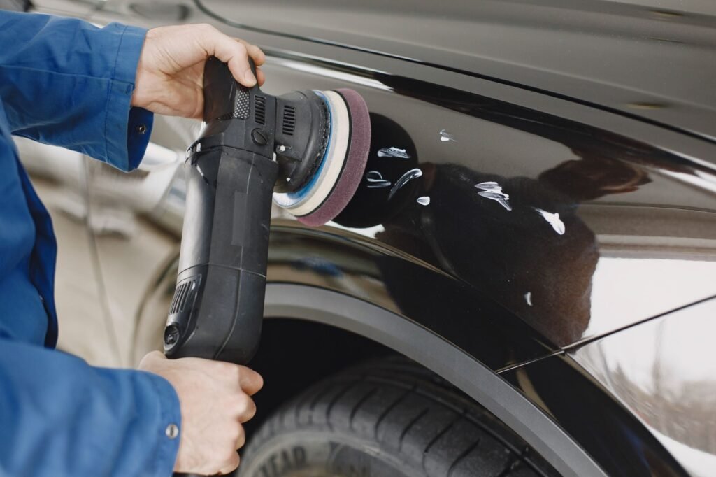 Person using a dual action polisher on the glossy black paint of a car