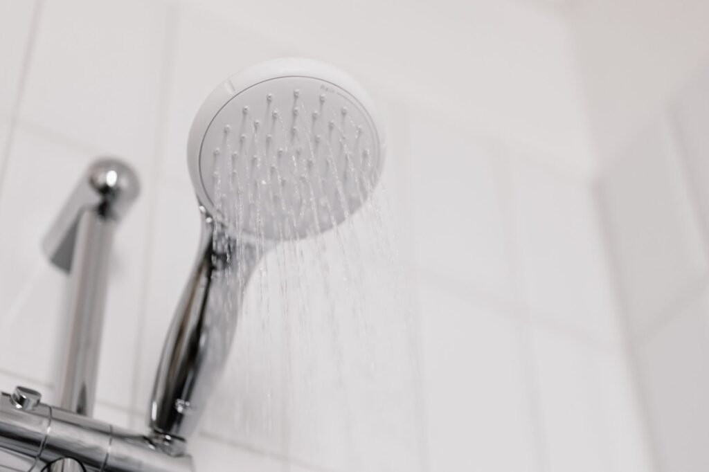 Handheld shower head spraying water beside a chrome shower valve on a white tiled wall