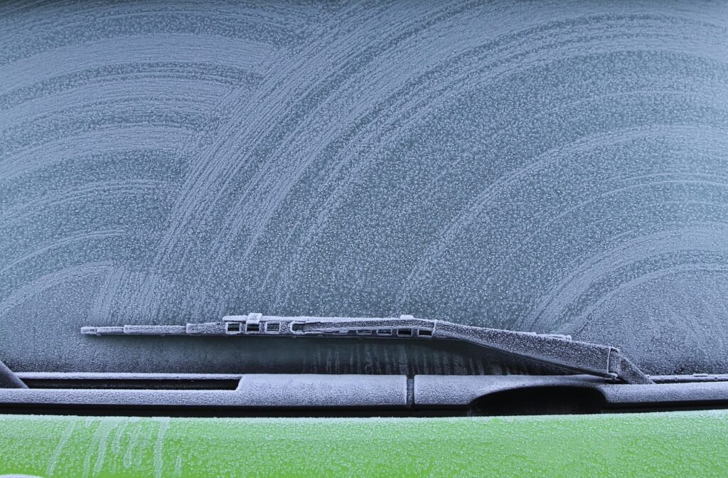 Close up of a windshield wiper blade resting at the base of a frosted windshield