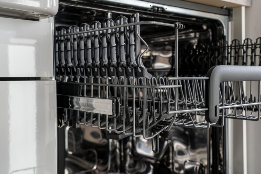 Open dishwasher with the top rack pulled out and an empty stainless steel interior