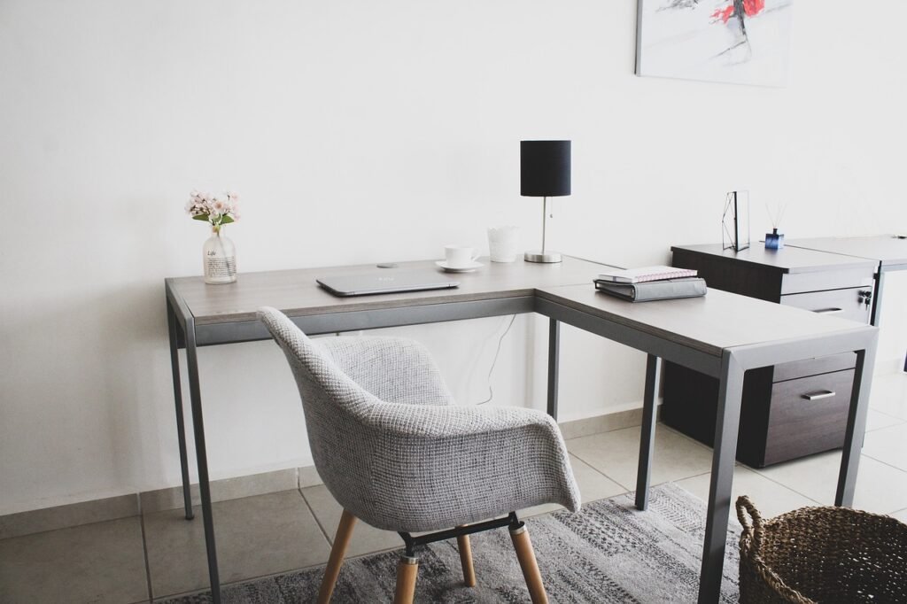 Gray upholstered chair at a corner desk with a lamp and small flower vase