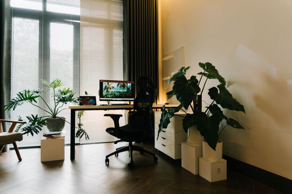 Sunlit home office with a black desk chair, computer monitor and potted plants by a window
