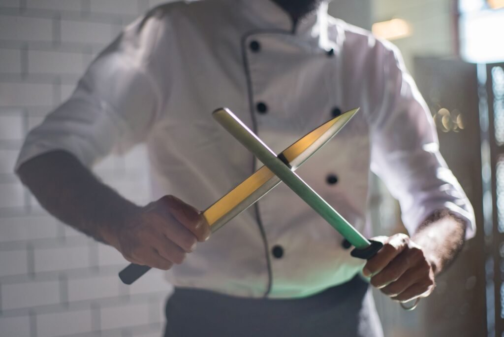 Cook in a white jacket drawing a chef knife across a honing steel
