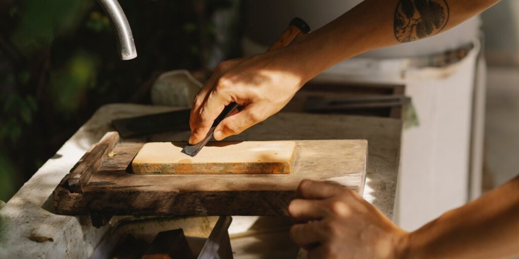 Hands sliding a knife blade across a sharpening stone set on a wooden base