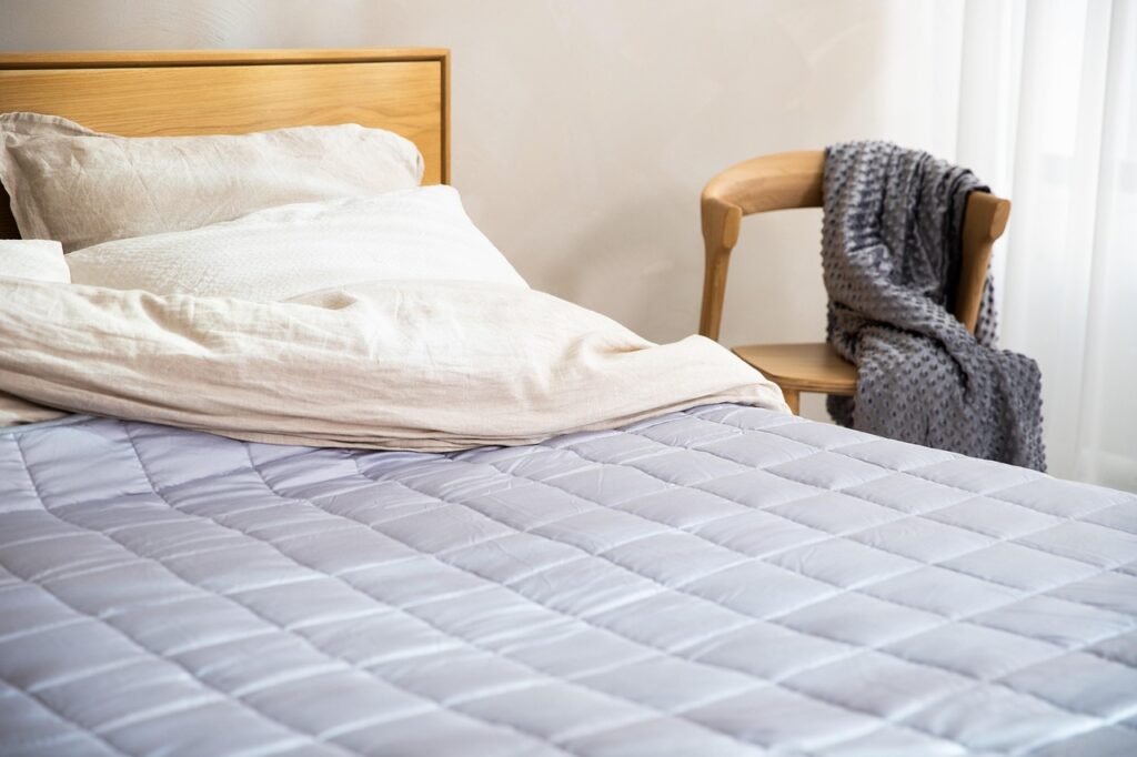 Neatly made bed with a quilted mattress cover, white pillows and a wooden headboard