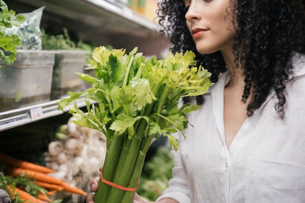 A woman examines a fresh bunch of celery in a produce aisle at the grocery store