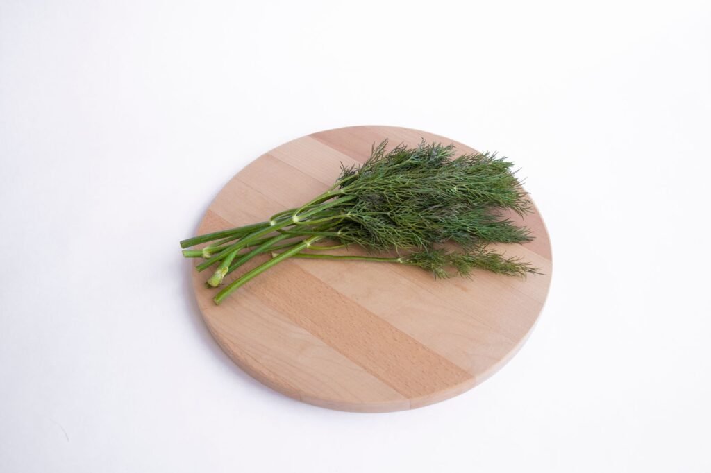 A close-up of fresh dill on a round wooden chopping board, ideal for culinary use