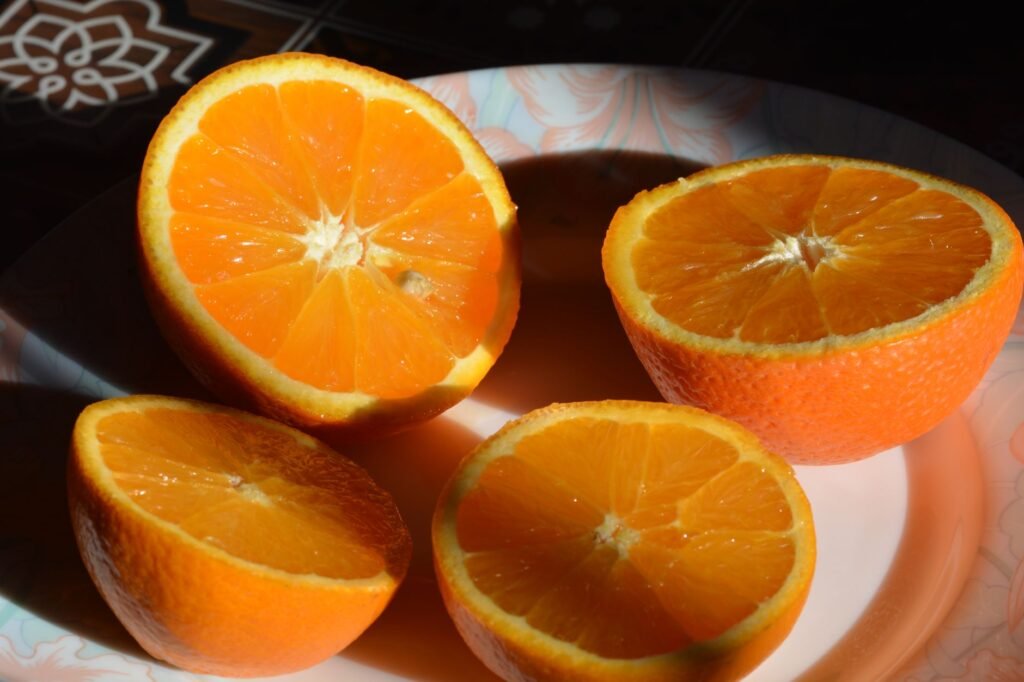 Close-up of juicy orange halves on a decorative plate with sunlight highlighting their vibrant color.