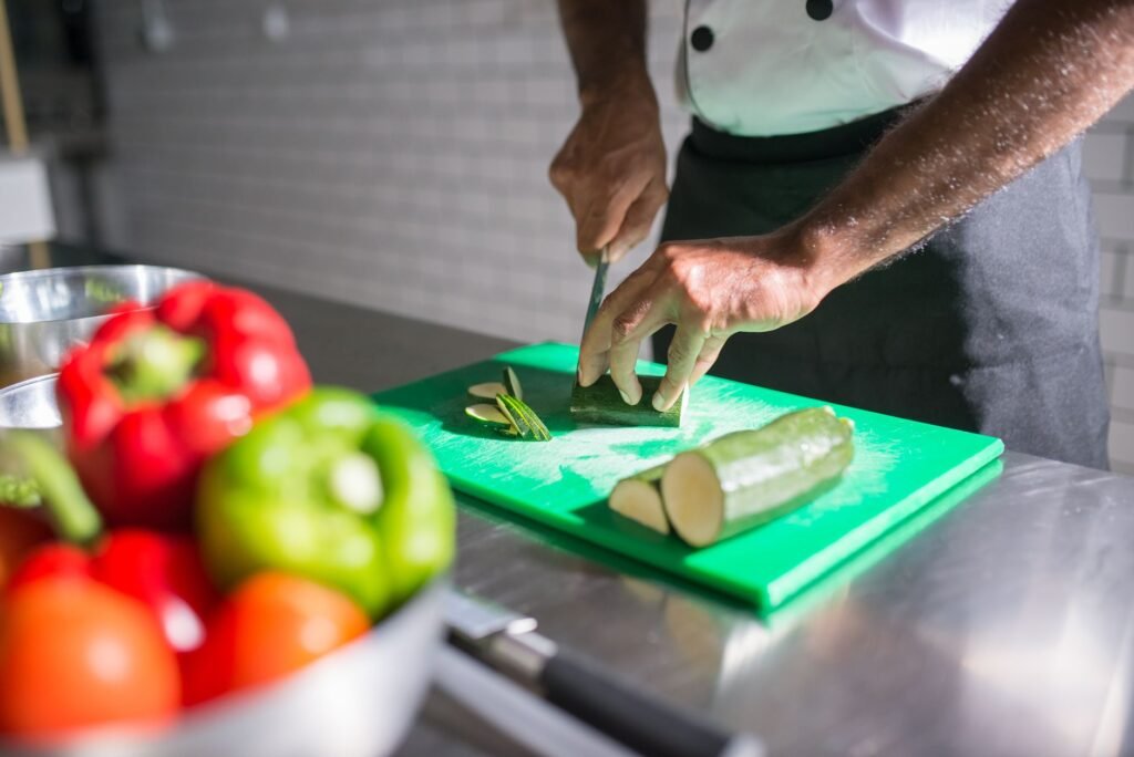Chef slicing zucchini on a green chopping board with fresh vegetables nearby