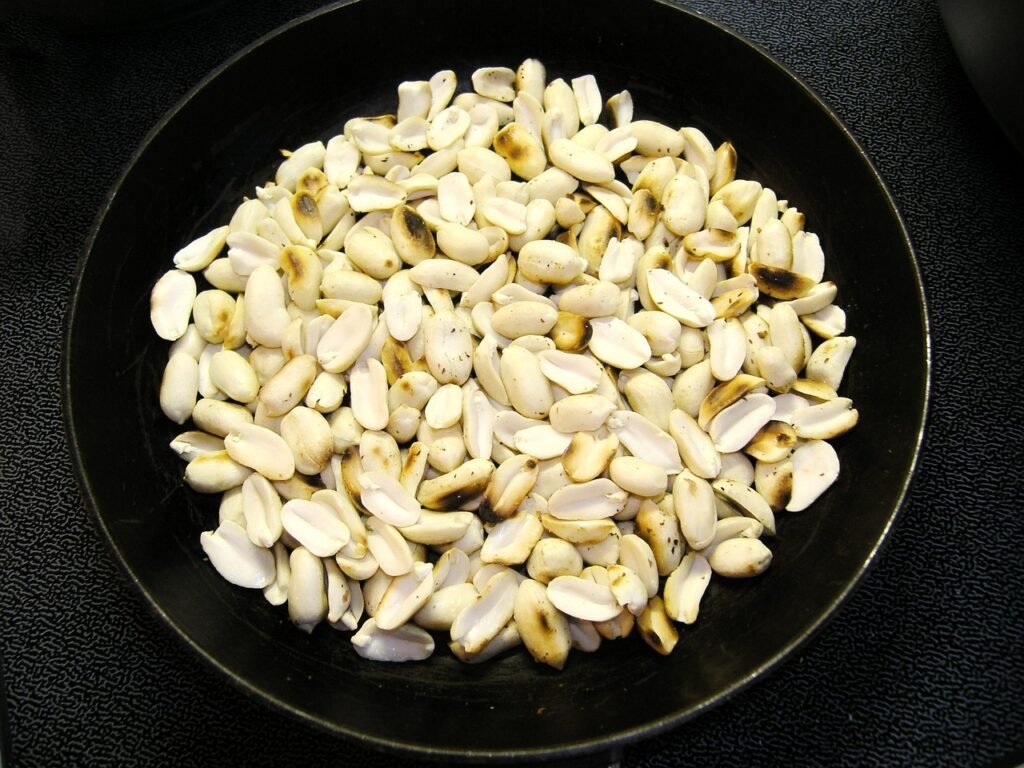 Shelled peanuts spread in a dark round pan on a black surface