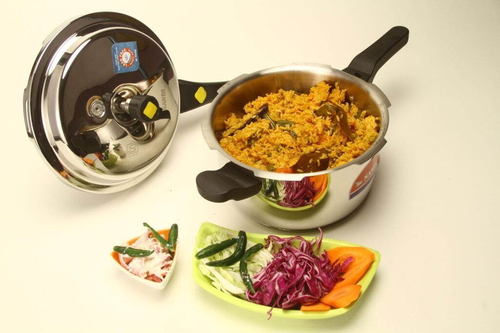 Open stovetop pressure cooker filled with vegetable rice beside its locking lid and sliced vegetables