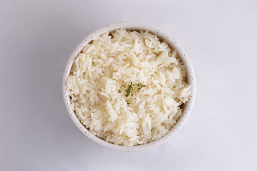 Bowl of fluffy cooked white rice topped with chopped herbs on a white surface