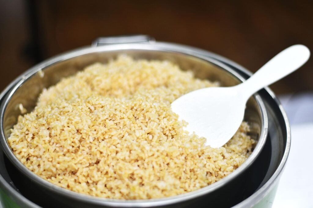 Freshly cooked rice in a stainless steel rice cooker pot with a white plastic paddle