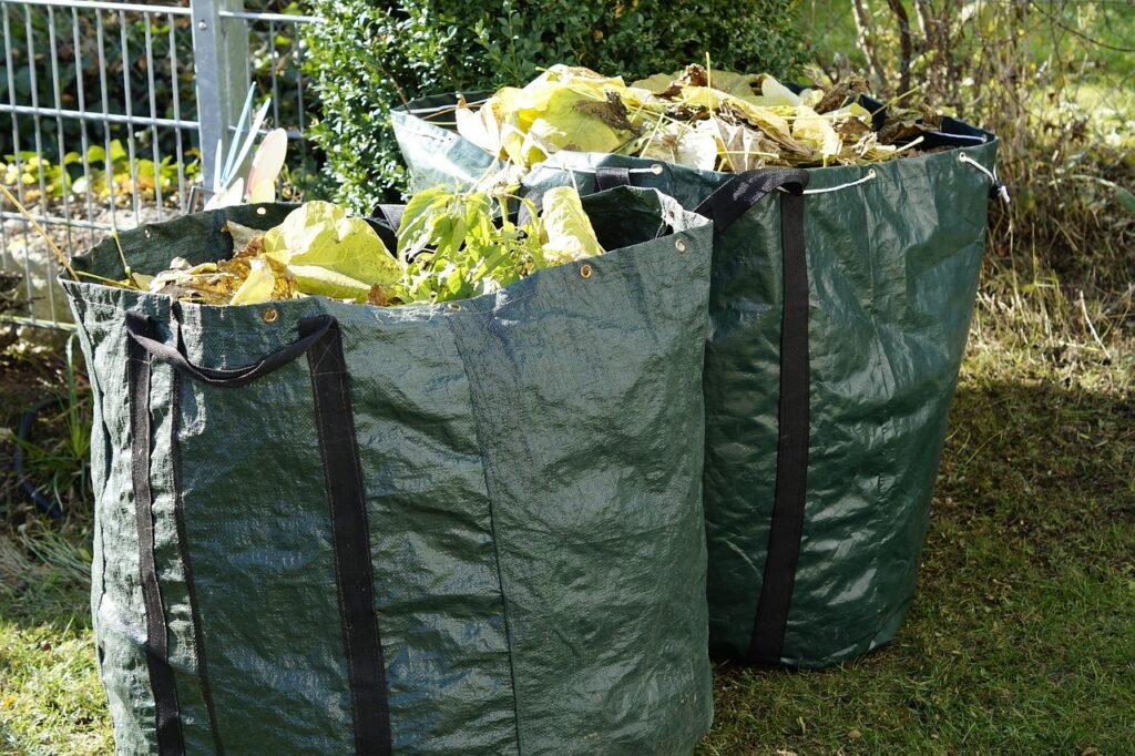 Two green garden waste bags filled with dry leaves and plant cuttings on a lawn