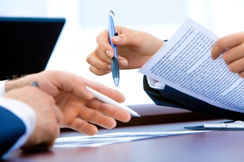 Two people reviewing a printed typed document with pens at an office desk