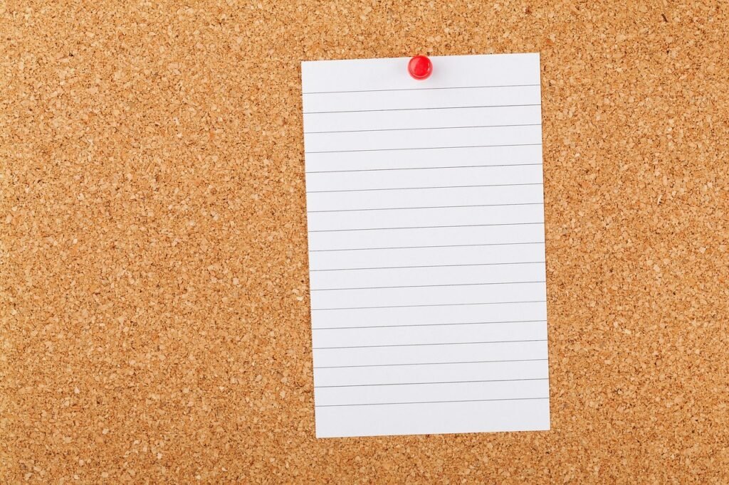 Blank lined notebook page pinned to a cork board with a red pushpin