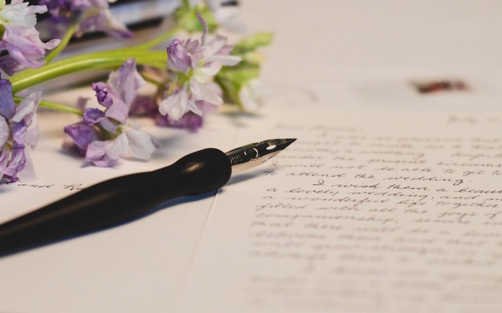 Black pen resting on a handwritten letter beside a sprig of purple flowers