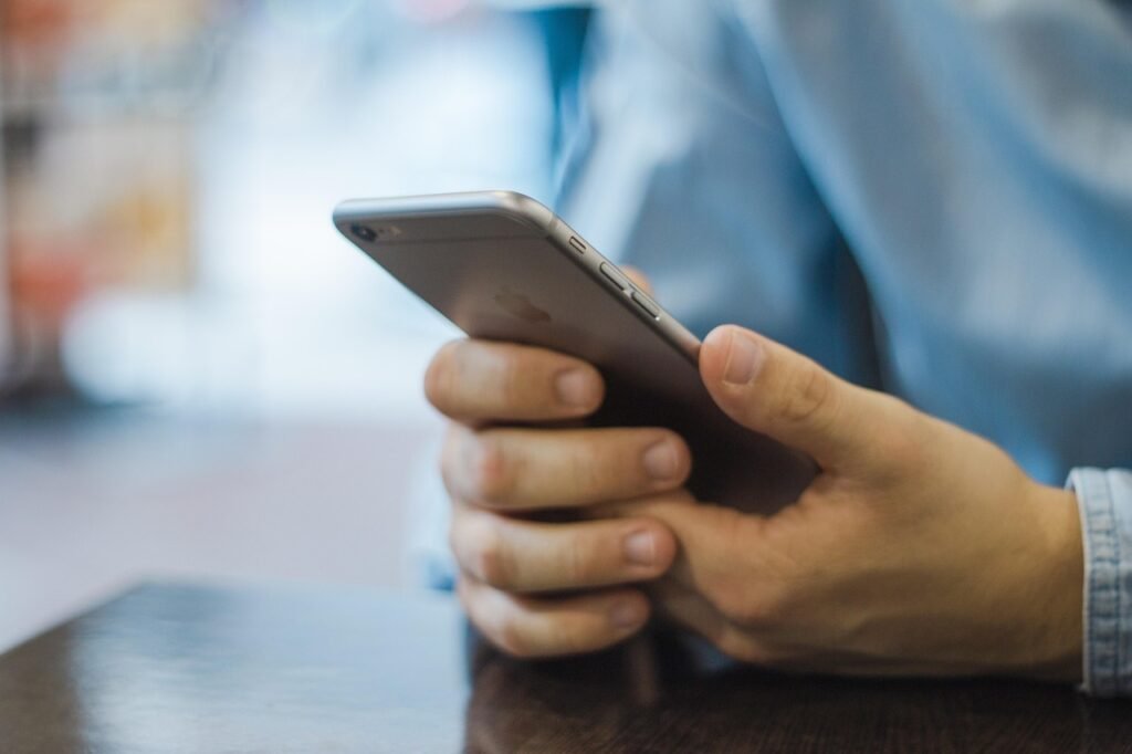 Person in a blue shirt holding a smartphone with both hands at a table