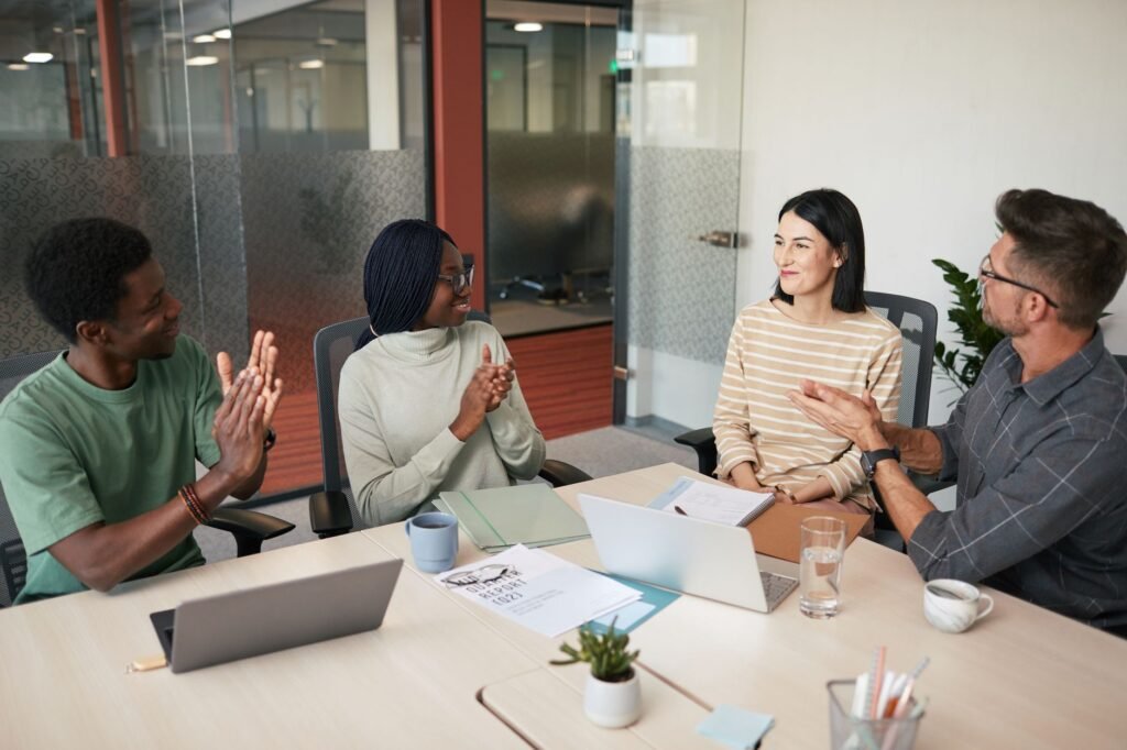 Small team of four talking around an office table with laptops and a potted plant
