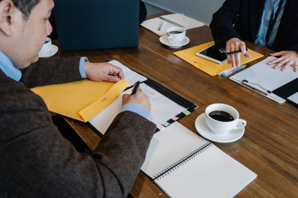 Coworkers at a wooden conference table with notebooks, papers, folders and coffee cups during a meeting