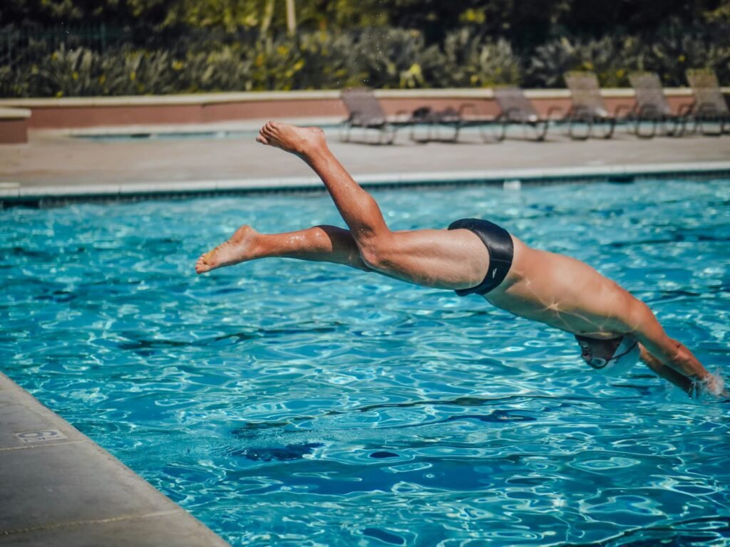 Swimmer in dark trunks diving headfirst toward the water of an outdoor pool