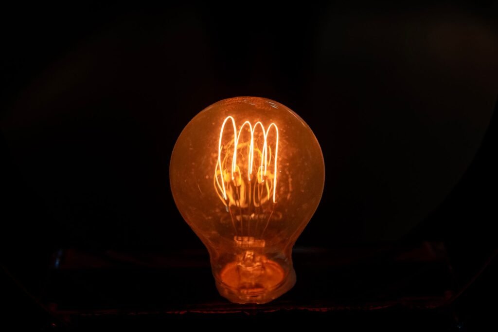 Clear glass light bulb with a glowing looped filament against a dark background