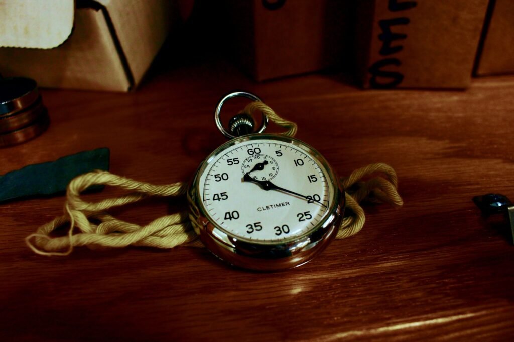 Mechanical stopwatch with a white dial and loop crown resting on a dark wooden table