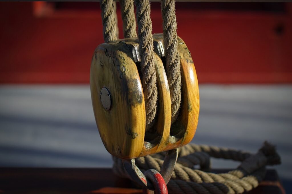 Wooden pulley block with thick rope threaded through it against a blurred red background