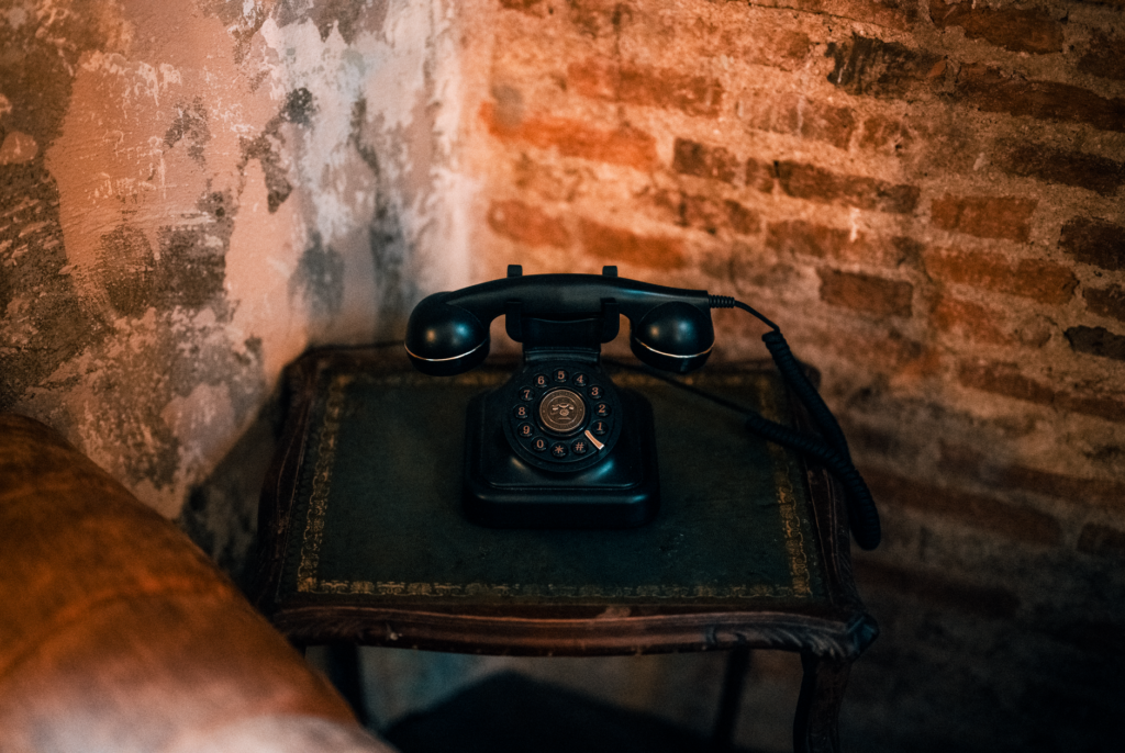 A classic black rotary telephone sits on an antique table by a brick wall, evoking nostalgia