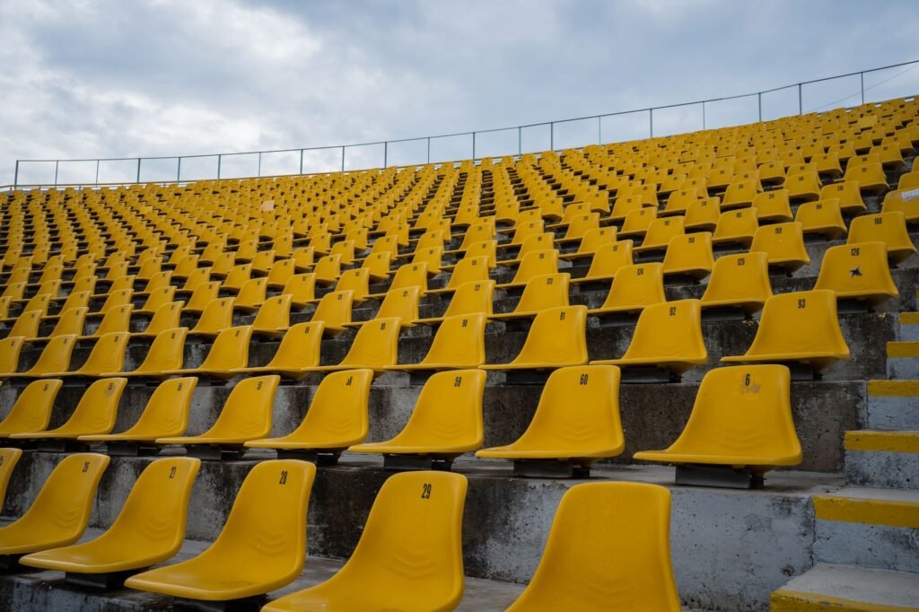 Rows of empty yellow plastic seats rising up a concrete stadium grandstand