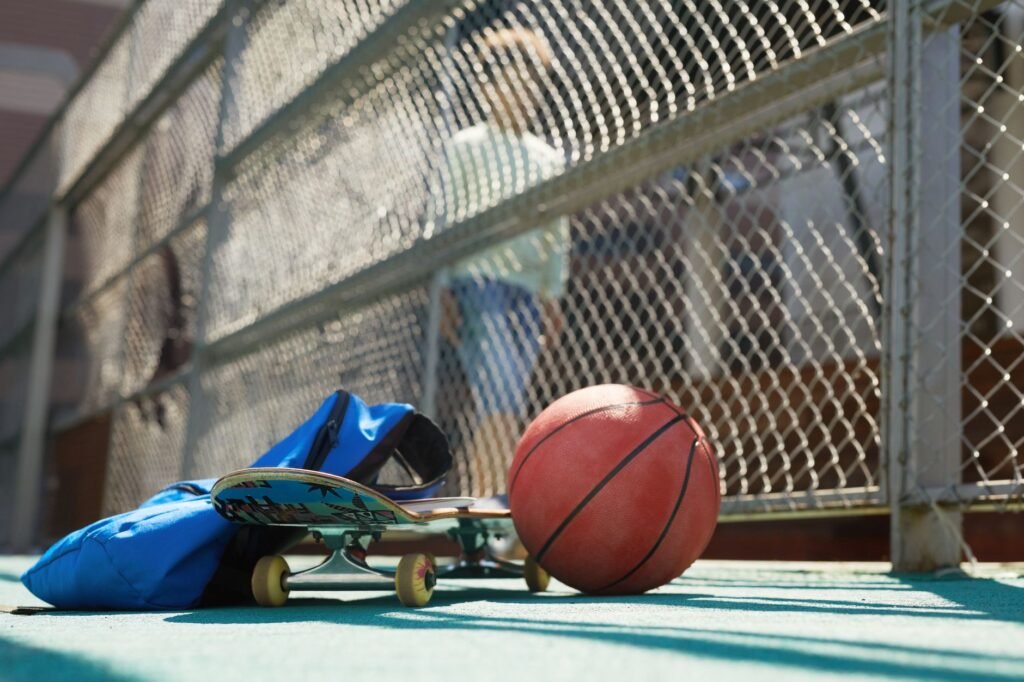 Skateboard, basketball, and blue bag placed near a chain-link fence, capturing active urban lifestyle