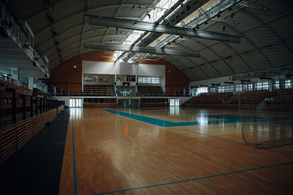Empty indoor sports arena with hardwood flooring and bleachers, perfect for various sports activities