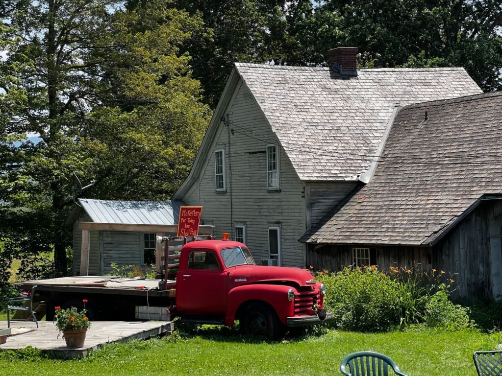 A charming vintage red truck parked by a rustic country house, surrounded by greenery