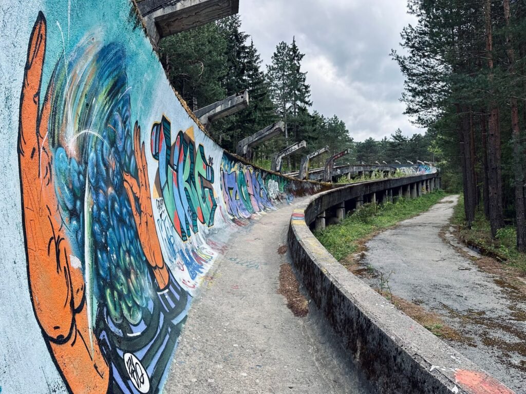 Vibrant graffiti on the abandoned Sarajevo bobsled track, surrounded by lush forest under a cloudy sky