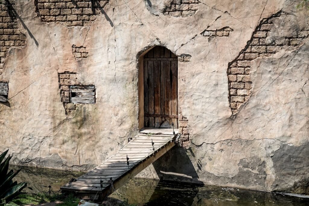 A weathered brick wall with a wooden door and a small wooden bridge over a pond