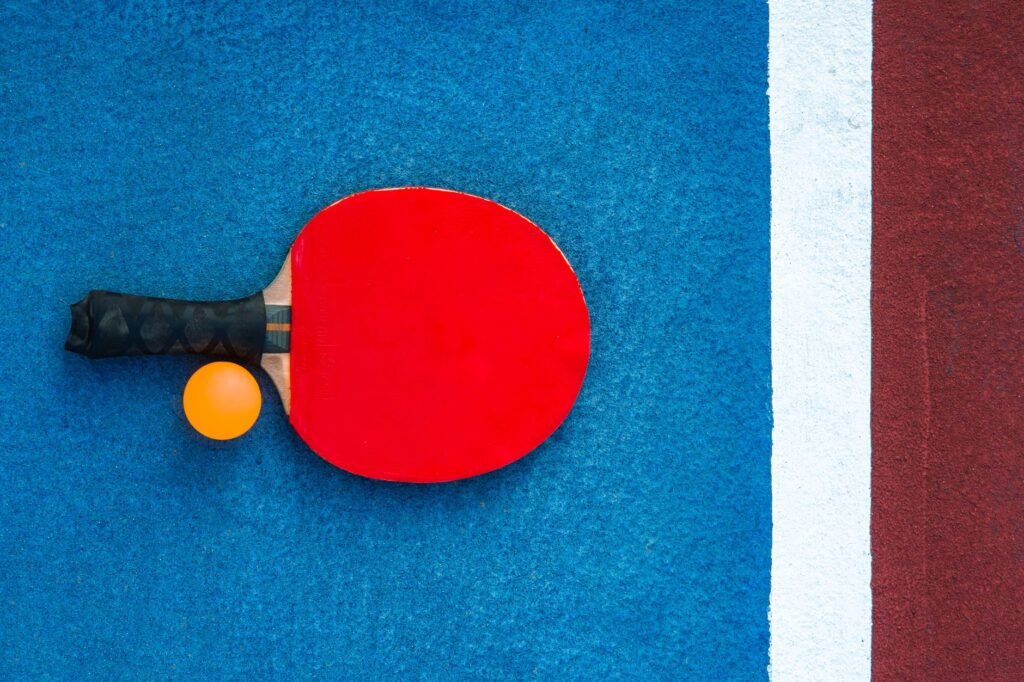A red table tennis paddle and orange ball on a colorful court background