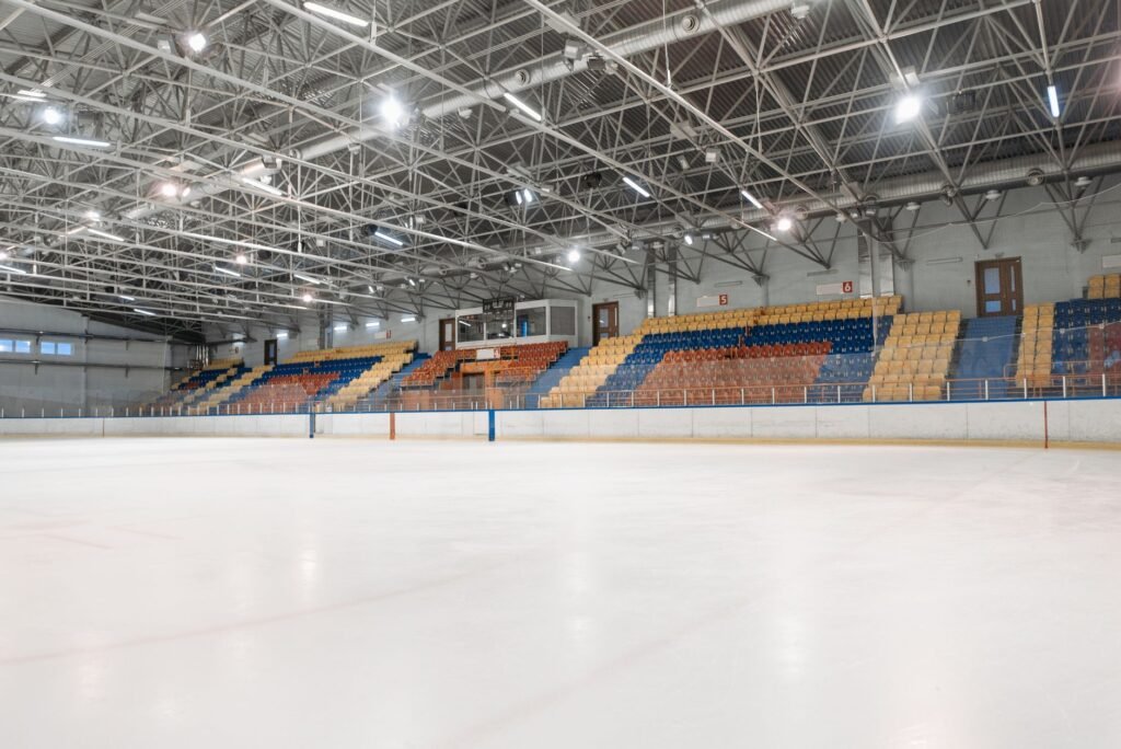 An empty indoor ice rink with tiered seating under an exposed steel roof