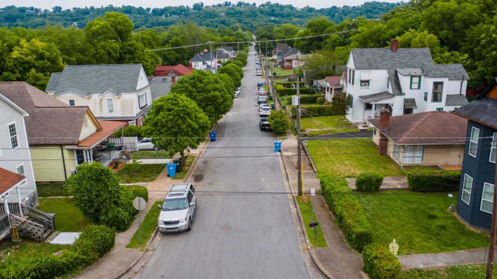 Explore a quiet suburban neighborhood street with houses and lush greenery from an aerial perspective