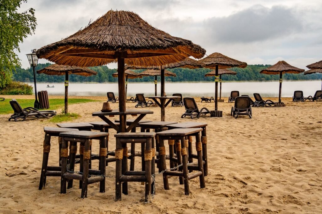 Quiet sandy beach with reed umbrellas and empty wooden stools, perfect for peaceful retreats.