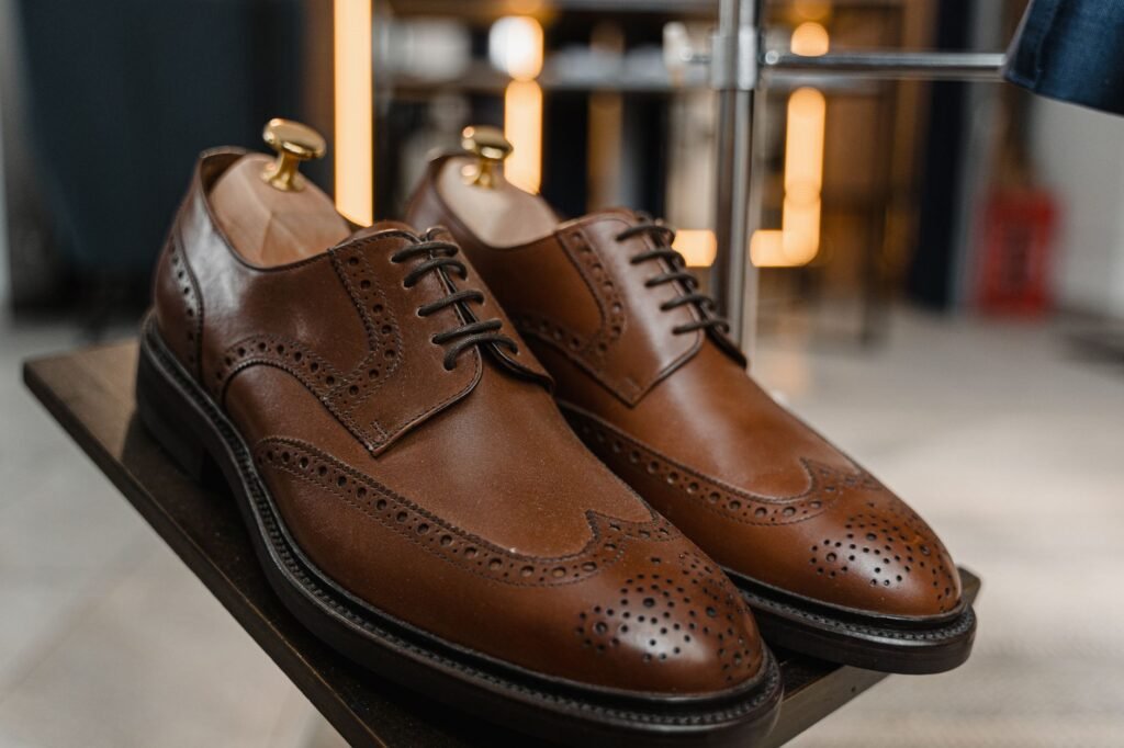 A pair of brown leather wingtip brogues with wooden shoe trees on a shop shelf