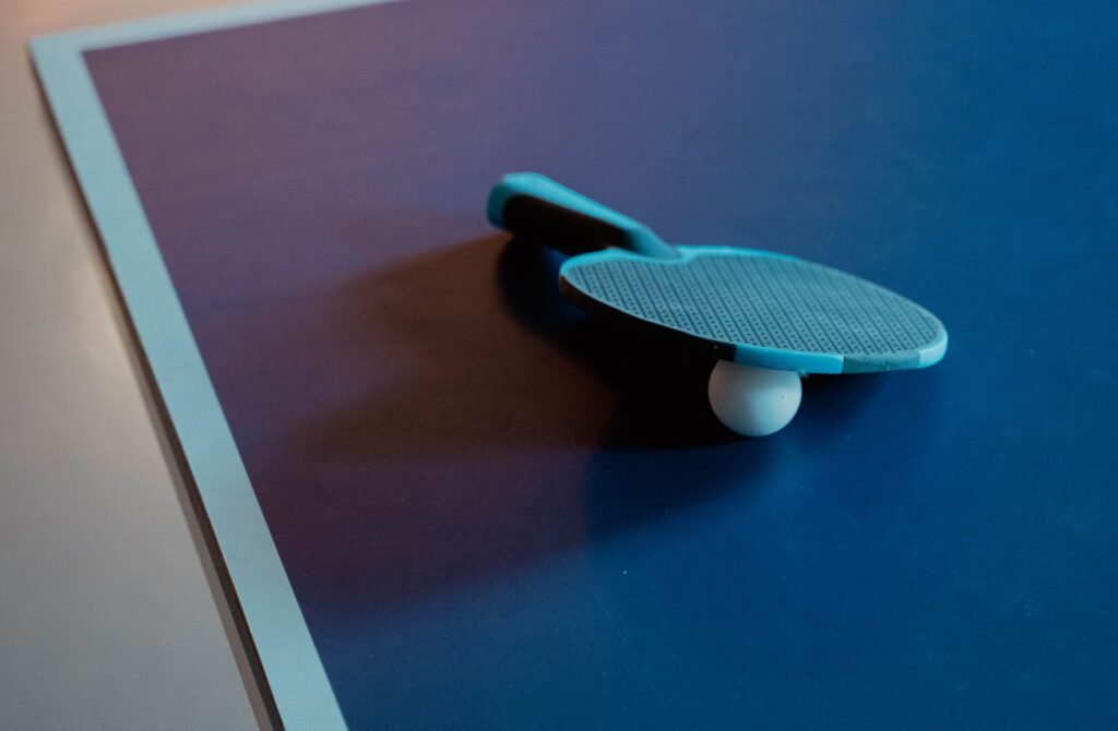 A table tennis paddle resting on a white ball at the corner of a dark blue table