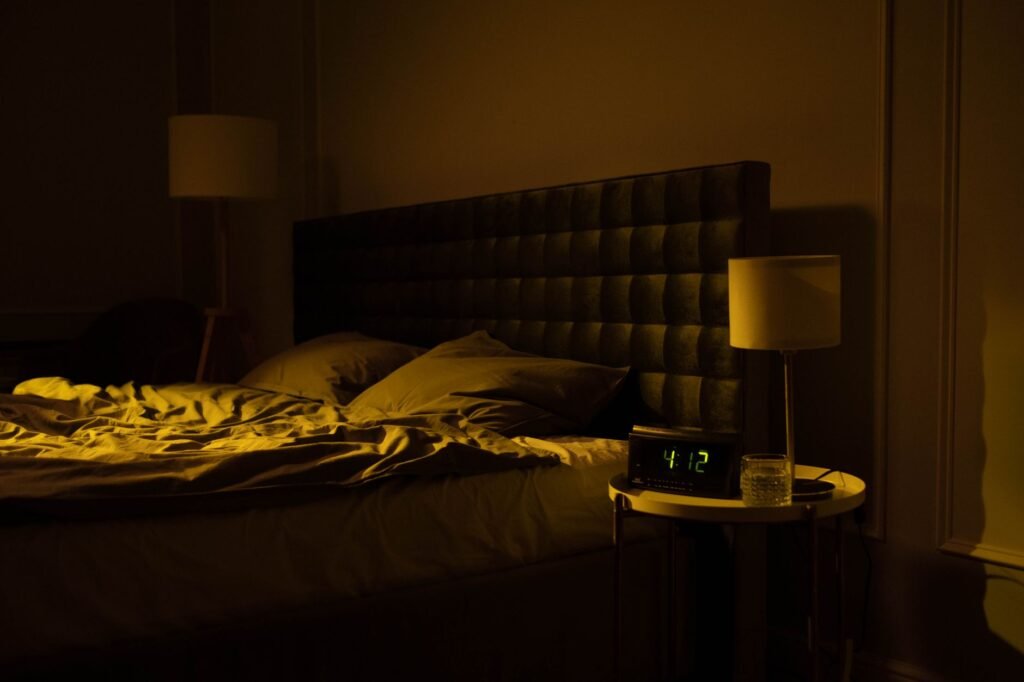 Relaxing dimly lit bedroom with an unmade bed, digital clock displaying 4:12, and warm ambient lighting