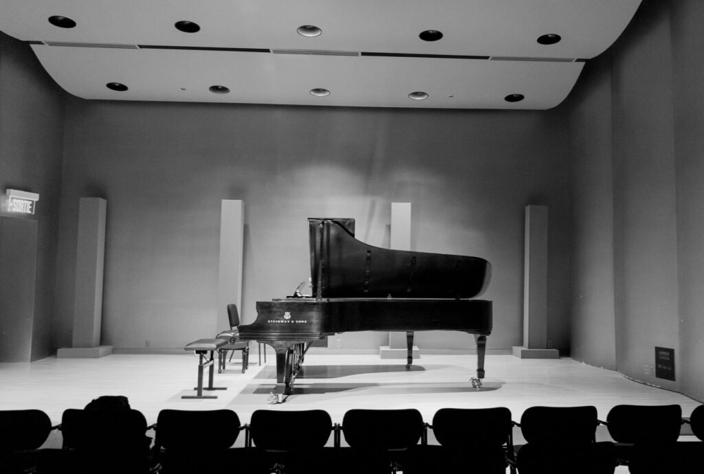 A grand piano with its lid raised standing alone on an empty stage