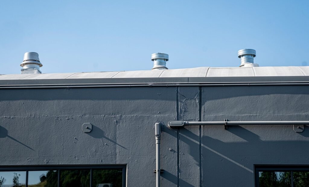 Three metal vent cowls along the parapet of a flat roofed building against a blue sky