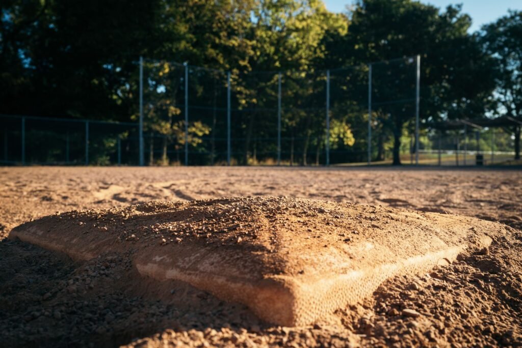 Close-up of a baseball base on an empty field with trees and fence in the background