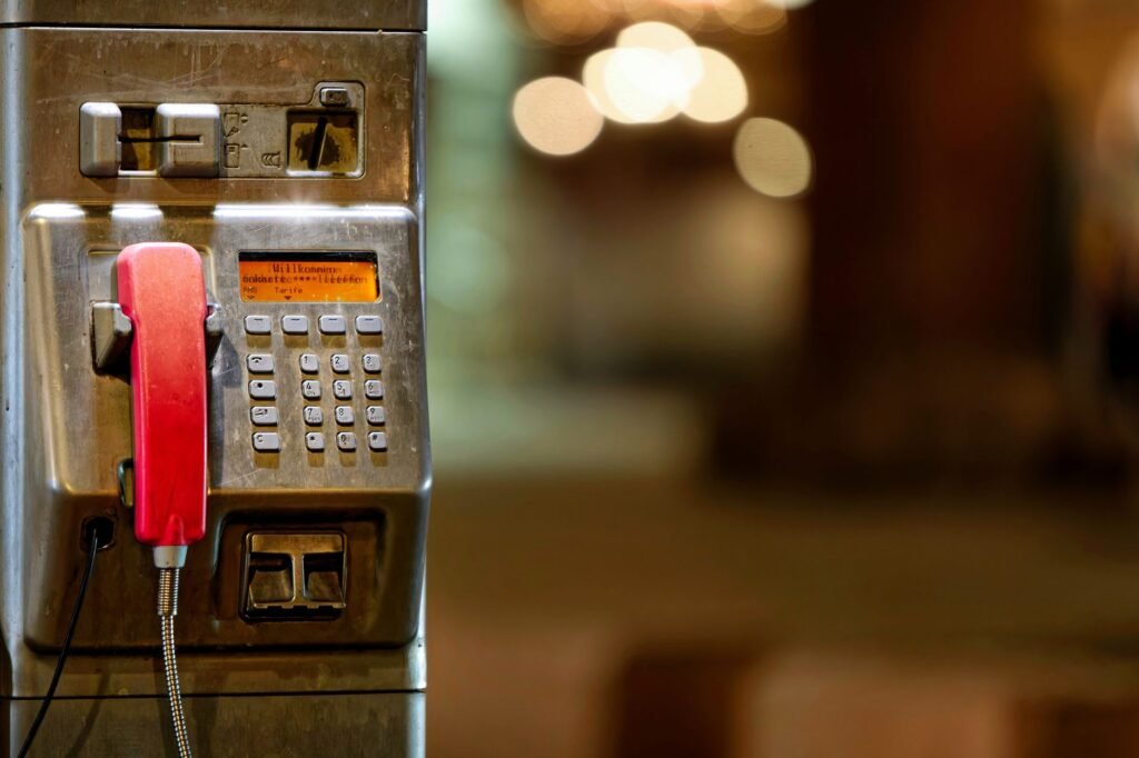 Vintage public telephone with red handset in an urban setting, blurred bokeh background