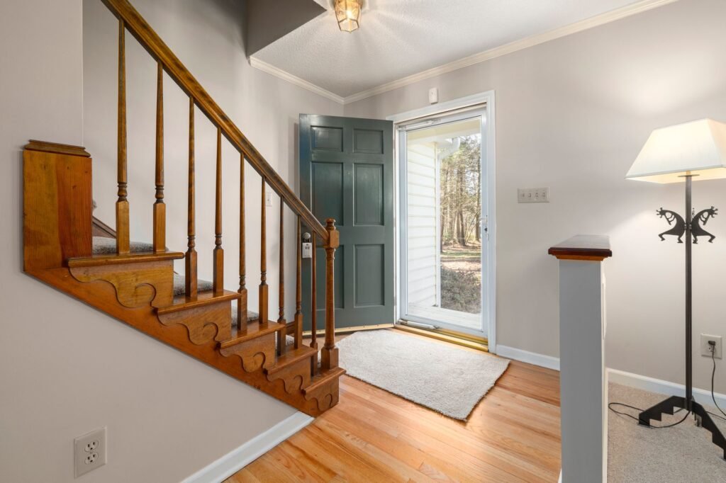 Inviting hallway with wooden staircase and open door leading to a sunny exterior