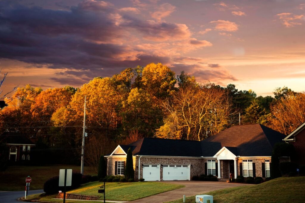 A picturesque suburban house surrounded by fall foliage under a dramatic sunset sky in Madison, AL