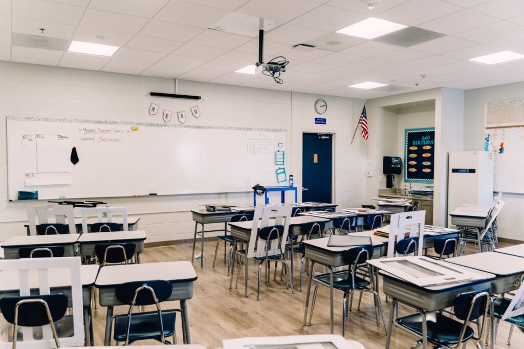 An empty classroom with rows of small student desks facing a long whiteboard