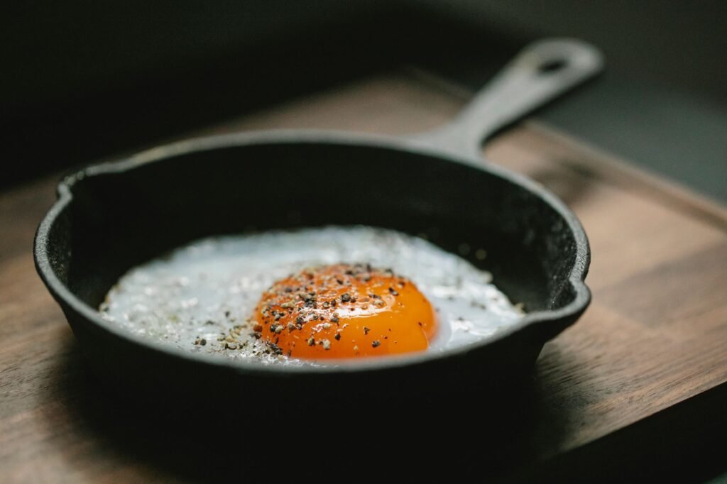 Fried egg with cracked pepper cooking in a black cast iron skillet on a wooden surface